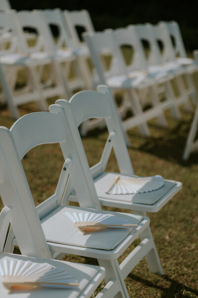 A beautiful and film-like photo of fans on white wedding chairs before a Coffs Harbour ceremony behind Annu