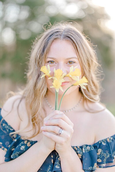 young girl, smiling at the camera with flowers front of her face