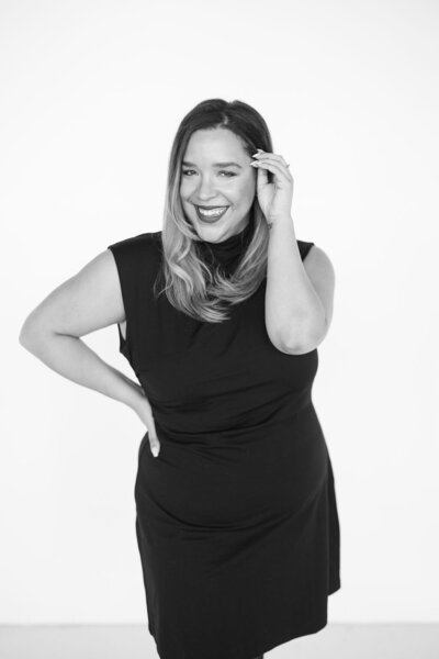 Natasha Churches, owner of Aisle & Co., poses for a headshot in all white while holding champagne.