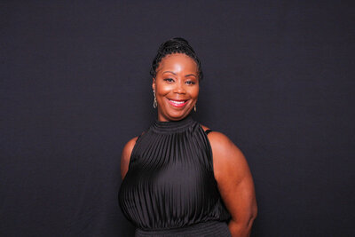 Woman in sleeveless black top posing confidently in front of a solid black backdrop.