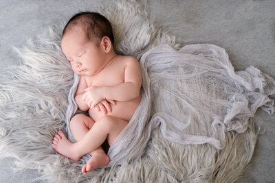 Newborn baby loosely wrapped in a gray blanket