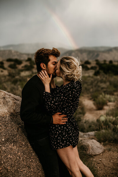engaged couple kissing in front of a rainbow in albuquerque