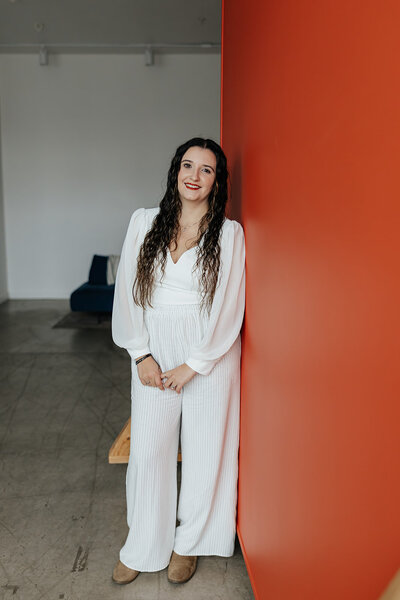 Taysha leaning against a red wall smiling at the camera.