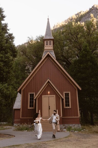 Bride and groom holding hands and running away from the Yosemite Chapel while smiling and laughing
