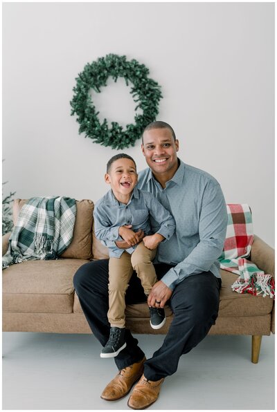a-dad-is-holding-his-son-on-his-lap-and-smiling-at-the-camera-for-christmas-studio-pictures-at-vow-collective-studios-by-nashville-family-photogarpher-dolly-delong