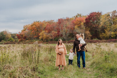 family with two kids and a pregnant mother walk in a field at sunset