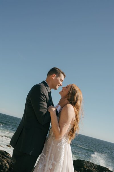 A bride and groom holding each other at a wedding in Maine with the ocean behind them.  