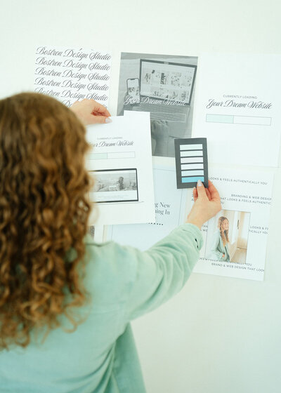 Haylee holding a color palette to a wall of branded pieces of paper. Her back is to the camera.