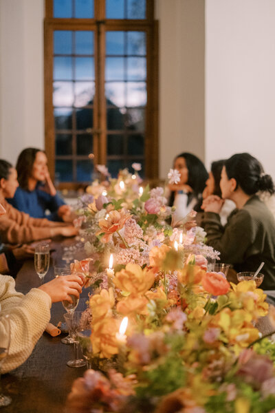 A long floral arrangement and candles decorate a table.