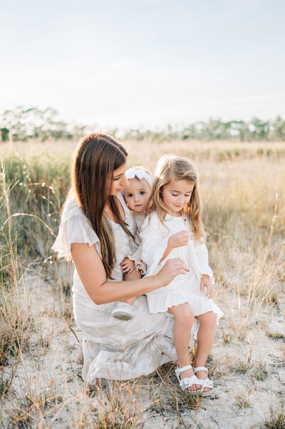 South Florida Family Photographer captures mom kneeling with her two daughters looking at a flower