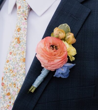 grooms boutonniere with pink ranunculus blue delphinium placed in a shoot gun shell