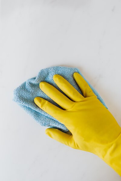 Main dans un gant jaune avec un chiffon bleu nettoyant une surface blanche