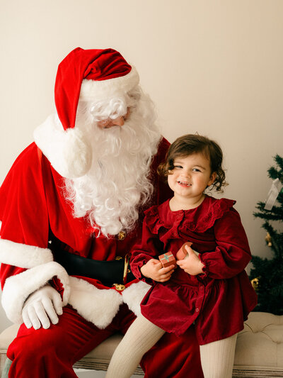 Little girl in a red dress sits in Santa's lap. 