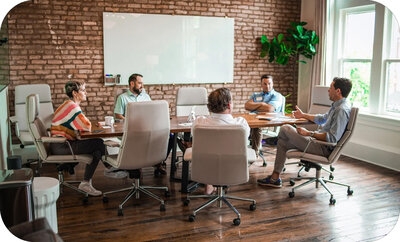 Group seated around a conference table in a brick-walled office, having a relaxed team discussion.