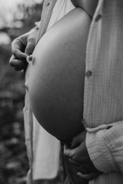 Schwarz weiss Bild von Babybauch von der Seite mit kleiner Blume