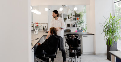 Brand photo for a hair salon featuring a hair stylist stylist the hair of his customer.