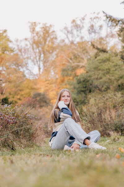 high school senior girl smiles at camera sitting on ground at connecticut college arboretum