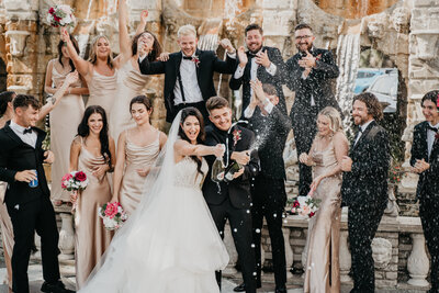 bride and groom with wedding party popping champagne