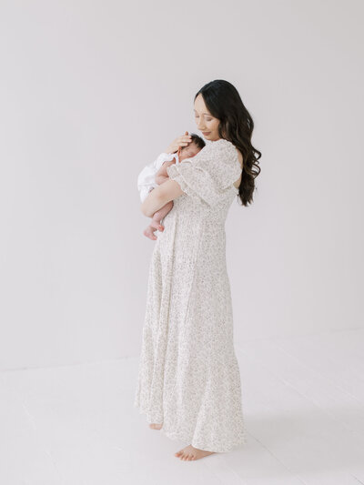 A mother wearing a flowing dress cradling her newborn in an all white studio in Seattle.