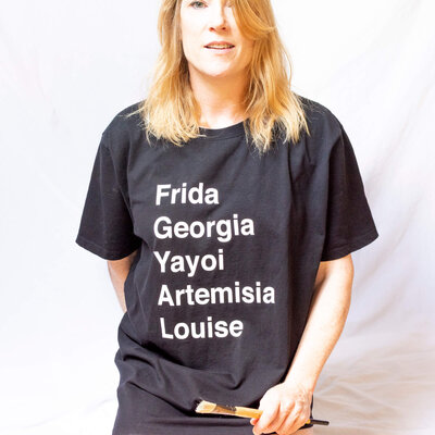 Henrie Richer wearing a shirt mentioning Frida, Georgia, Yayoi, Artemisia, Louise and holding a paint brush