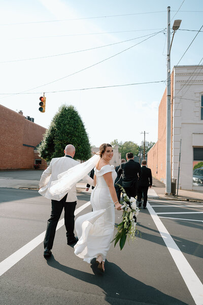 Urban love: Bride and groom strolling hand in hand through the city streets, capturing a candid moment with the bride's veil dancing in the breeze