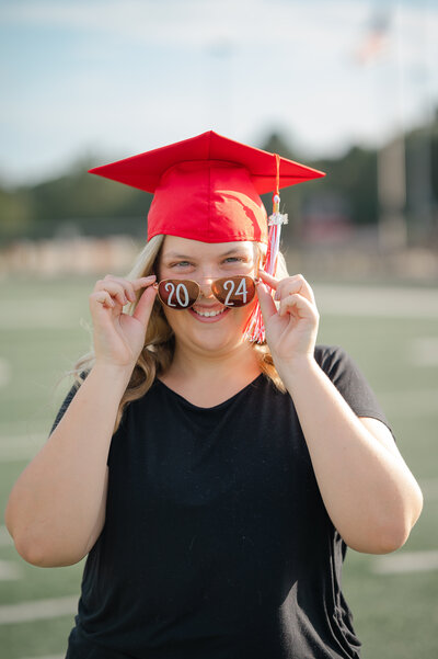 High school senior holds edges of her hat and smiles during senior photos in Monroe, Georgia