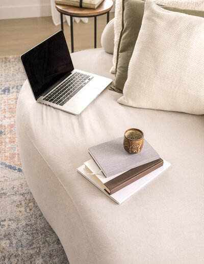 Laptop on a couch next to a stck of books
