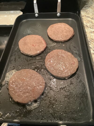 Four bratwurst patties on frying pan