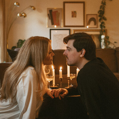 A couple gazing into each other’s eyes, surrounded by the warm glow of candles in their home.