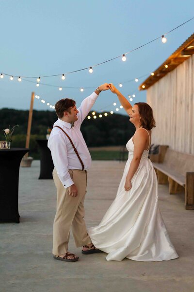 bride and groom dancing together in the evening with string lights in the background