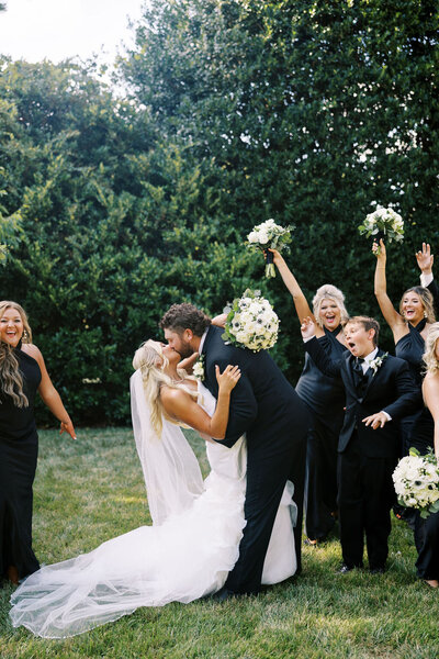 Kaiela and Zach hold hands on the lawn of Boxwood Estate. Kailea is wearing a white gown with her hair down, holding a white bouquet. Zach is wearing a classic black tuxedo with a white rose boutonnière on his left side.  