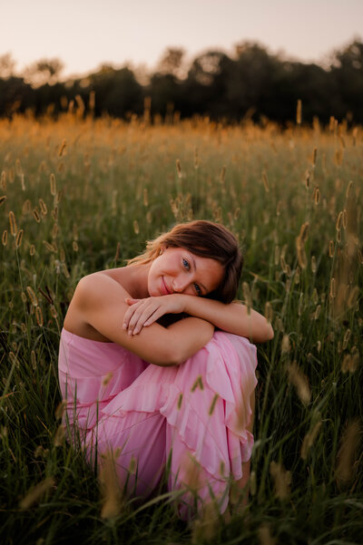 Girl in pink dress kneels in field.