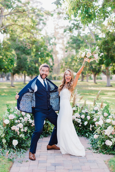 Elegant Wedding Firestone Vineyard Los Olivos - a bride and groom embrace in a kiss, with a classic car behind them and the sun setting over the vineyards in the distance