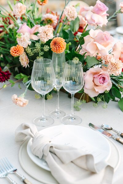 table setting featuring stone colored linens and pink + orange floral centerpiece
