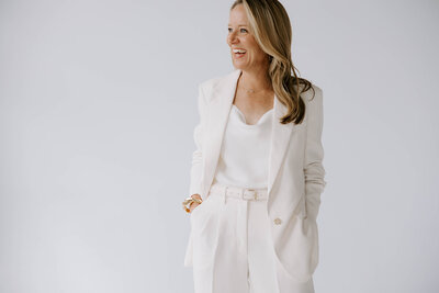 Heather Frick executive coach in a white business suit standing in front of a white wall