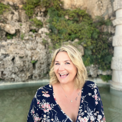 Maggie Dickens, LPCS, smiling outdoors in a floral dress, representing a feminist therapist who helps women who feel “too much” find relief from anxiety, burnout, and people-pleasing.