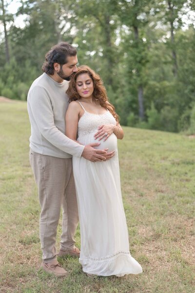 Expecting parents share a quiet embrace in a lush outdoor setting, capturing the anticipation of their baby. A maternity session by Moments in Light Photography.
