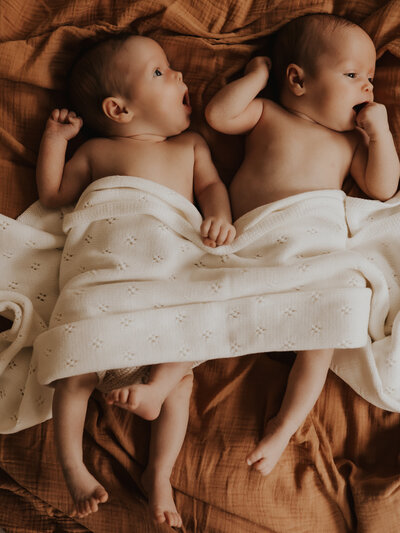 Gorgeous twin baby girls covered with a white wrap for their in-home photoshoot