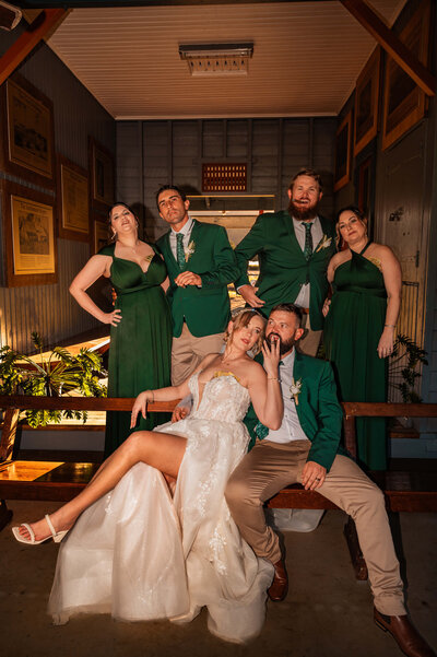 A bride and groom stand proudly with their wedding party, all smiling and celebrating their special day together.