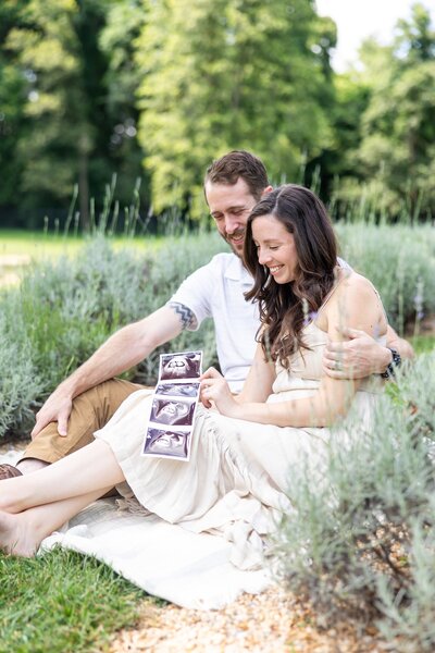 Expecting parents sitting in a filed admiring ultrasound photos