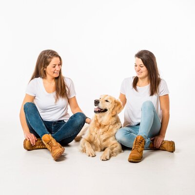 2 braunhaarige Mädchen sitzen auf dem Boden mit einem Golden Retriever