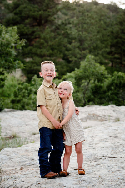 A toddler boy stands hugging and holding hands with his little sister