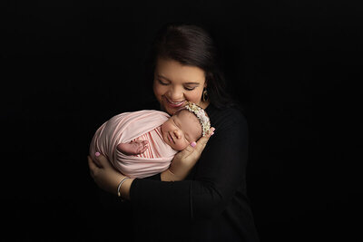 A happy mother cradles her smiling sleeping newborn baby daughter in her hands in a studio