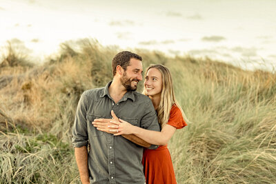 A man and a woman embracing in an outdoor setting for an engagement photoshoot. They are both smiling and appear to be happy and in love.