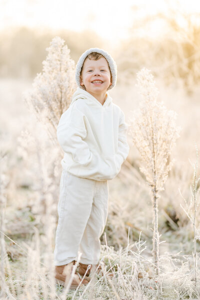 Gezinsshoot in de natuur bij ochtenddauw: kind in winterkleding tussen het bevroren groen met ijskristallen, sfeervol vastgelegd door Juliette Fotografie.