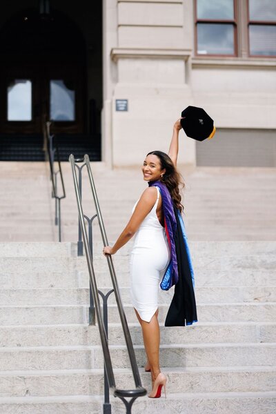 A graduation photo of a woman standing on a stairs posing and smiling for the camera