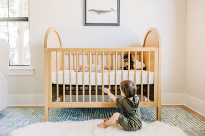 Big brother admires baby brother in the crib. In home light bright photography near St. Pete