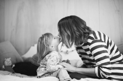 Mother and daughter sharing a kiss on the bed, a loving family photoshoot in Sydney.