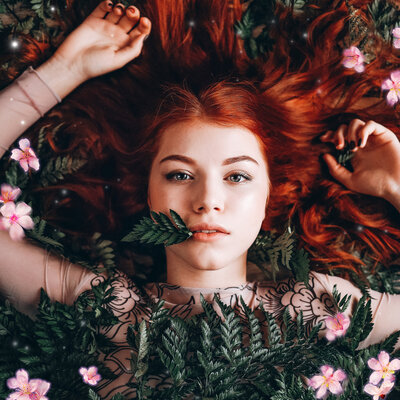 girl with red hair lying amongst ferns and flowers
