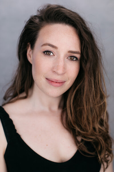 Castingfoto van musicalzangeres Janis Van Dorsselaer. Lang bruin haar, zwarte top en zelfverzekerde glimlach.